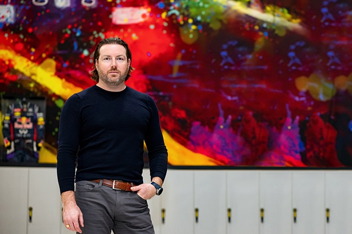 Adam Spencer standing in front of a multi-coloured abstract painted wall